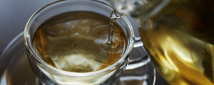 imagem aproximada de um bule de chá colocando chá em uma xícara em cima de mesa