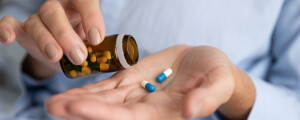 Mãos femininas e frasco de medicamentos com duas cápsulas brancas e azuis sob as mãos