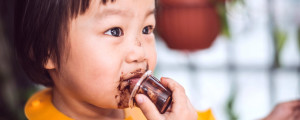 Bebê com pote de chocolate na mão segurando perto da boca