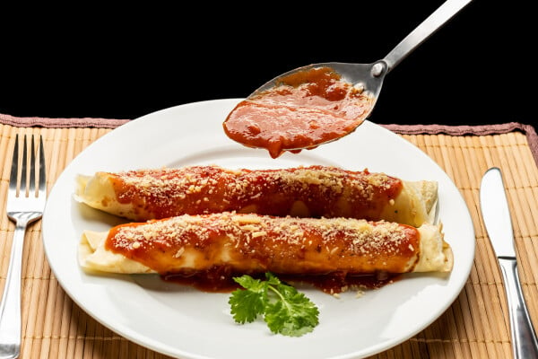 duas panquecas de pão integral com molho de tomate em prato branco, com talheres ao lado