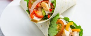 Wraps dentro de um prato branco com recheio de tomates, alface, cebola, peru; tomates ao redor