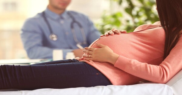 Mulher grávida deitada em maca e um médico está sentado ao lado