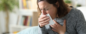 Mulher sentada em sofá tossindo enquanto cobre a boca com papel branco