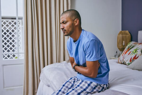 Homem com dor de barriga sentado na cama
