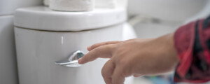 pessoa dando descarga em vaso sanitário branco com papel higiênico em cima