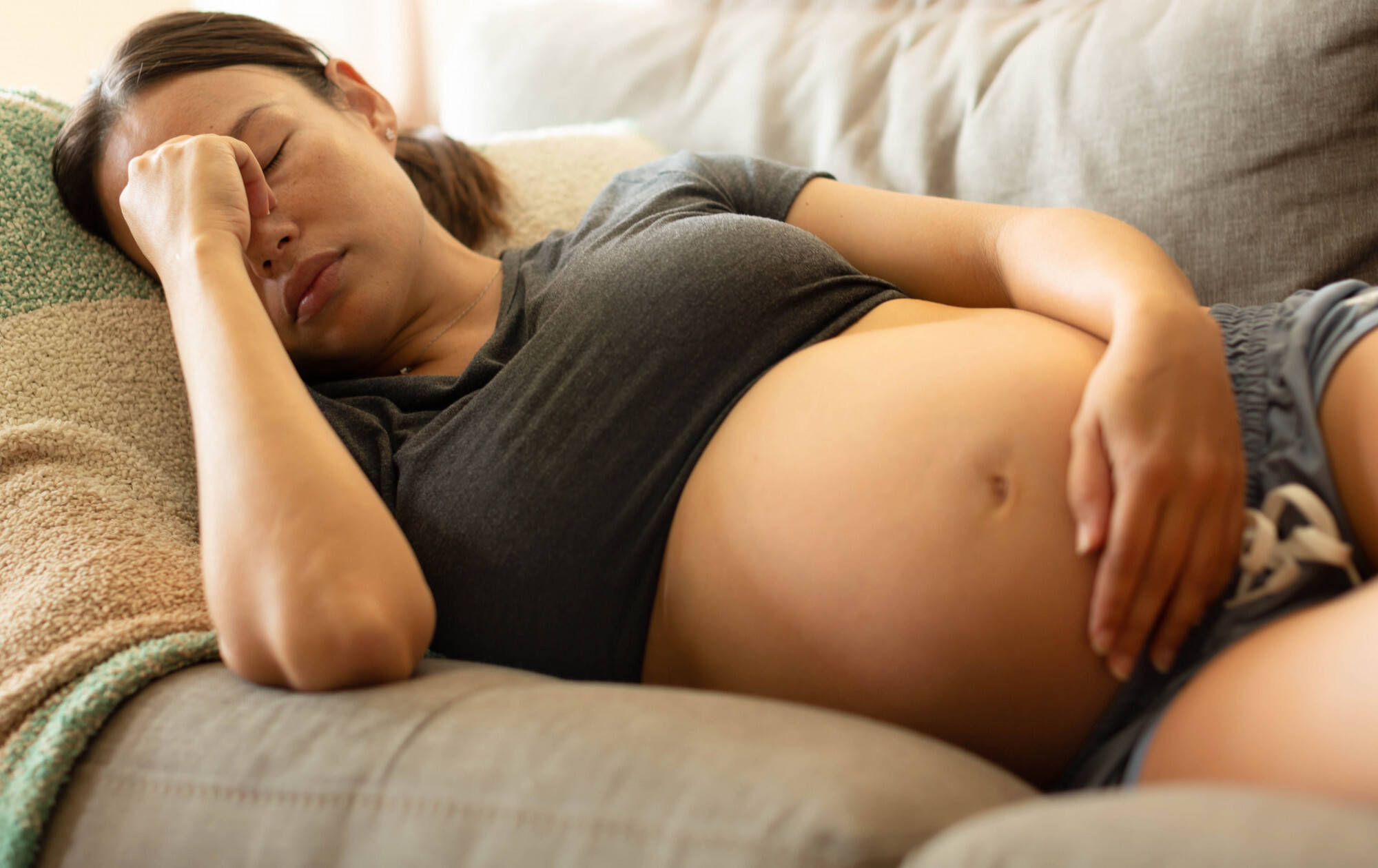 Mulher grávida deitada em um sofá com dor de cabeça