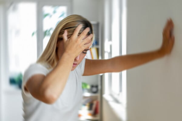 mulher sentindo tontura com a mão na cabeça e uma mão na parede