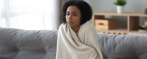 Mulher sentada no sofá enrolada em um cobertor sentindo frio