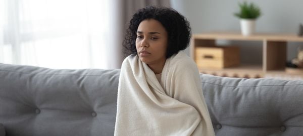 Mulher sentada no sofá enrolada em um cobertor sentindo frio