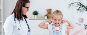 Criança pousando fazendo "muques" com o braço enquanto é avaliada por pediatra