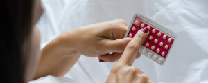 Foto aproximada de mulher segurando uma cartela de pílula anticoncepcional
