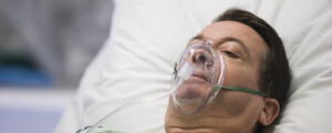Homem deitado em uma maca, com uma mascará de oxigênio no rosto, enquanto faz oxigenioterapia