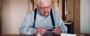 Homem idoso segurando uma cartela de comprimidos sentado em uma mesa