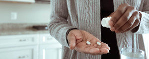 Mulher com dois comprimidos de antibióticos na mão.