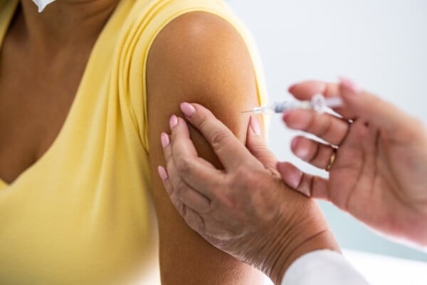 Close de braço de uma mulher recebendo a vacina da gripe