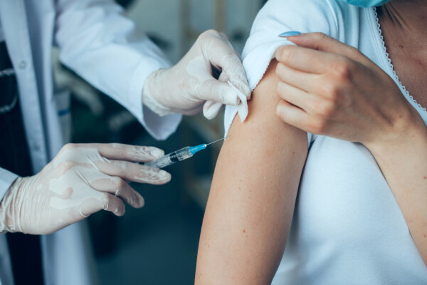 pessoa recebendo uma vacina no braço por um médico enquanto levanta a manga da blusa