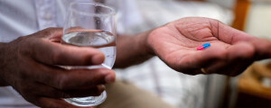 imagem aproximada de um homem segurando um copo de água e um comprimido