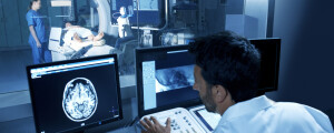 médico em uma pequena sala olhando para um angiograma. na frente da sala, há um paciente deitado em uma máquina de raio x, realizando uma angiografia