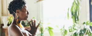 Mulher meditando com as palmas das mãos unidas em um estúdio de yoga, com plantas ao fundo