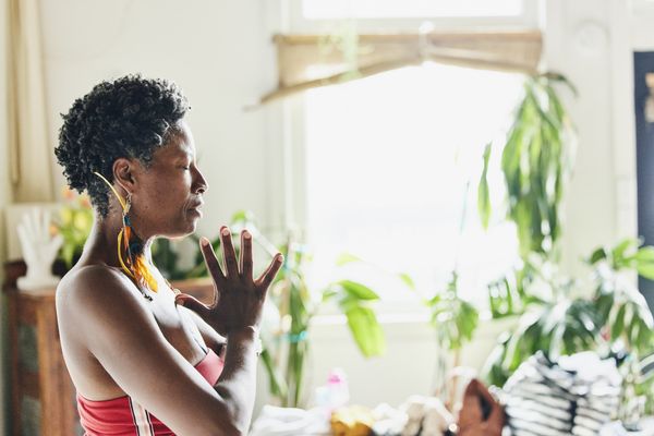 Mulher meditando com as palmas das mãos unidas em um estúdio de yoga, com plantas ao fundo