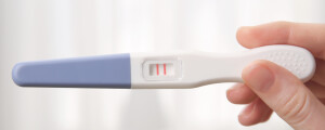 Mão feminina segurando um teste de gravidez positivo